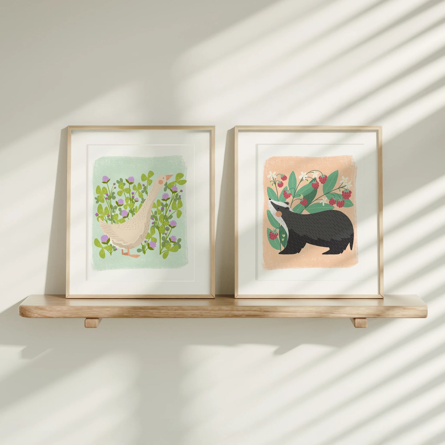 two cute animal art prints shown framed on a wooden ledge. on the left a goose and on the right a badger.