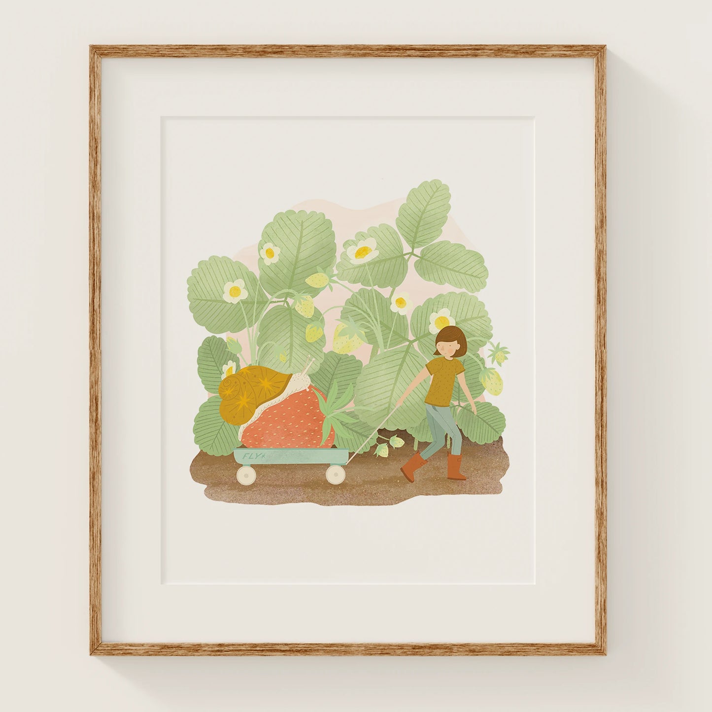 along for the ride art print, shown in a wood frame. print features a kid pulling a wagon with a strawberry inside on top of the strawberry is a snail. in the background are strawberry plants.