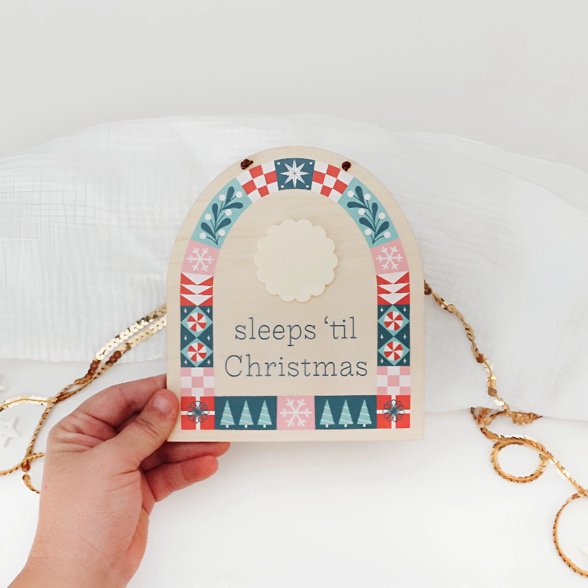 wood countdown sign with 'sleeps 'til Christmas' text and decorative patterns shown hanging on a white background being held by a hand.