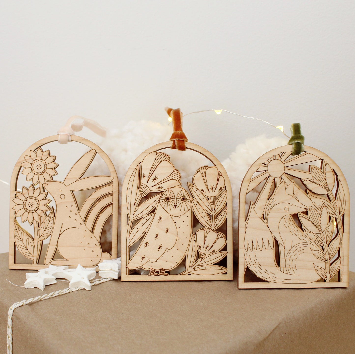 collection of wooden arch shaped insect ornaments with intricately etched designs: from left to right a rabbit, owl and fox, resting on a gift box