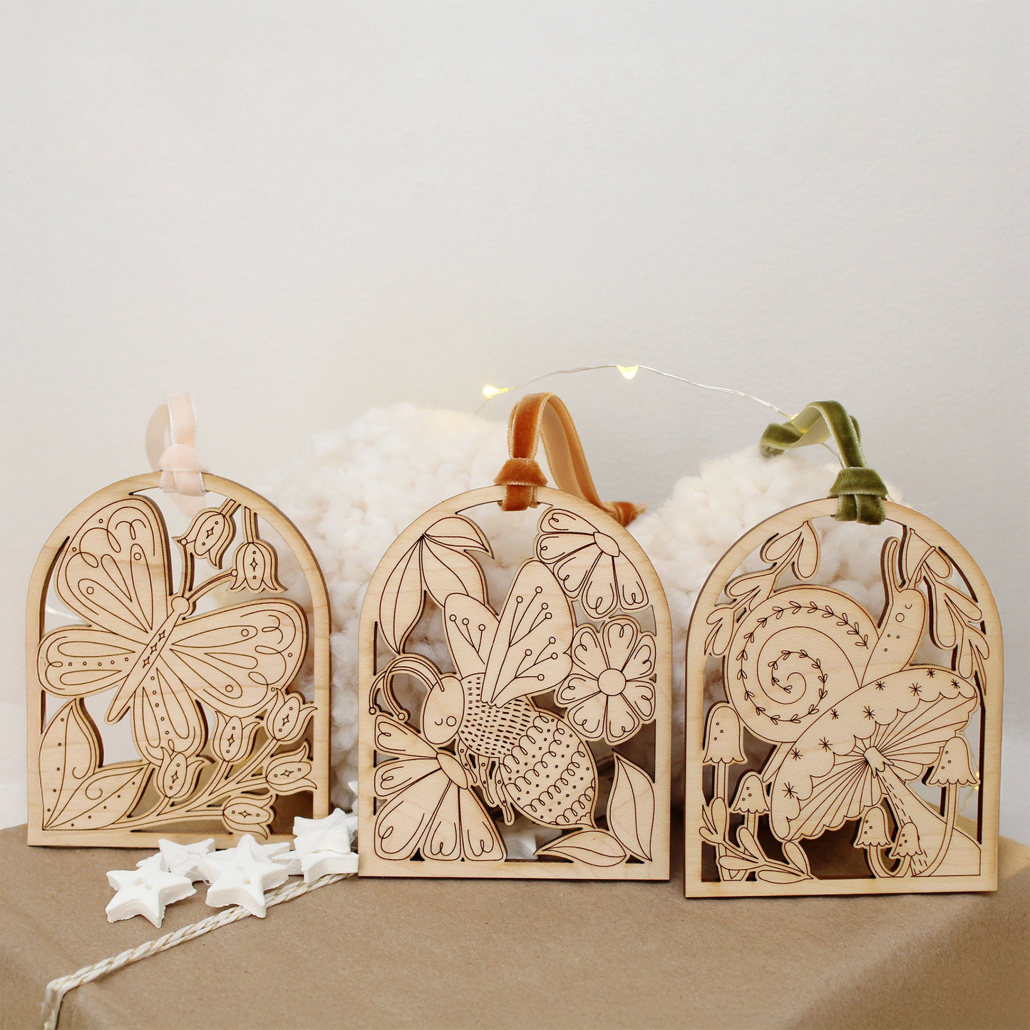collection of wooden arch shaped insect ornaments with intricately etched designs: from left to right a butterfly, bee and snail, resting on a gift box