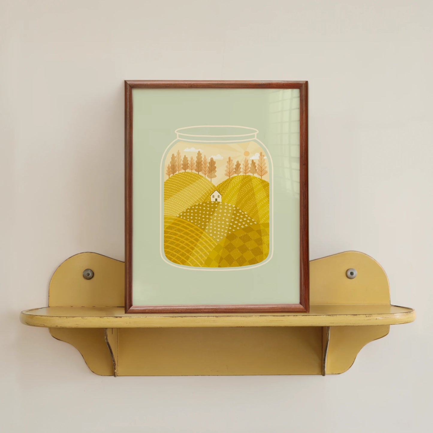 'going home' art print, shown in a wood frame on a yellow shelf. print features a small white house nestled among yellow fields during a peach sunset, inside of a jar.