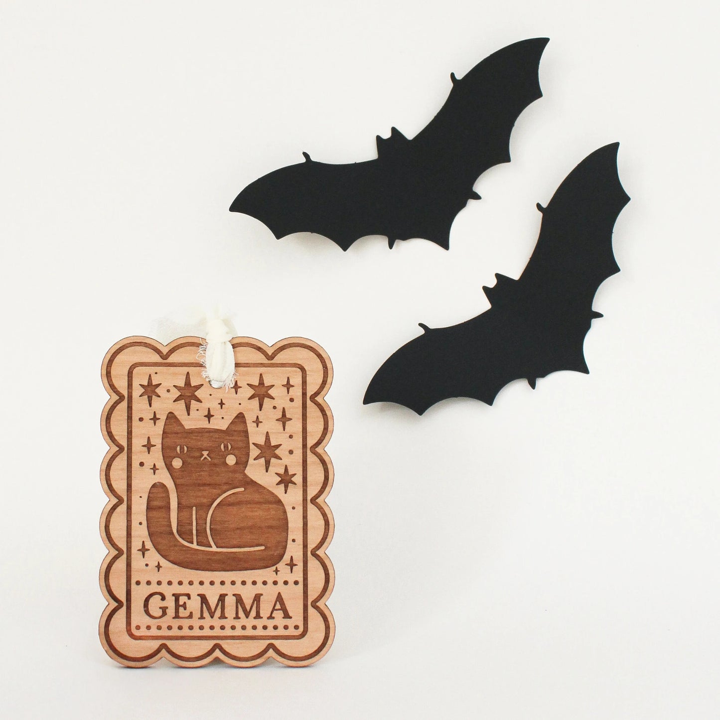 personalized halloween tags with black cat design propped up in front of white background with two black bats. tag is customized with the name GEMMA.