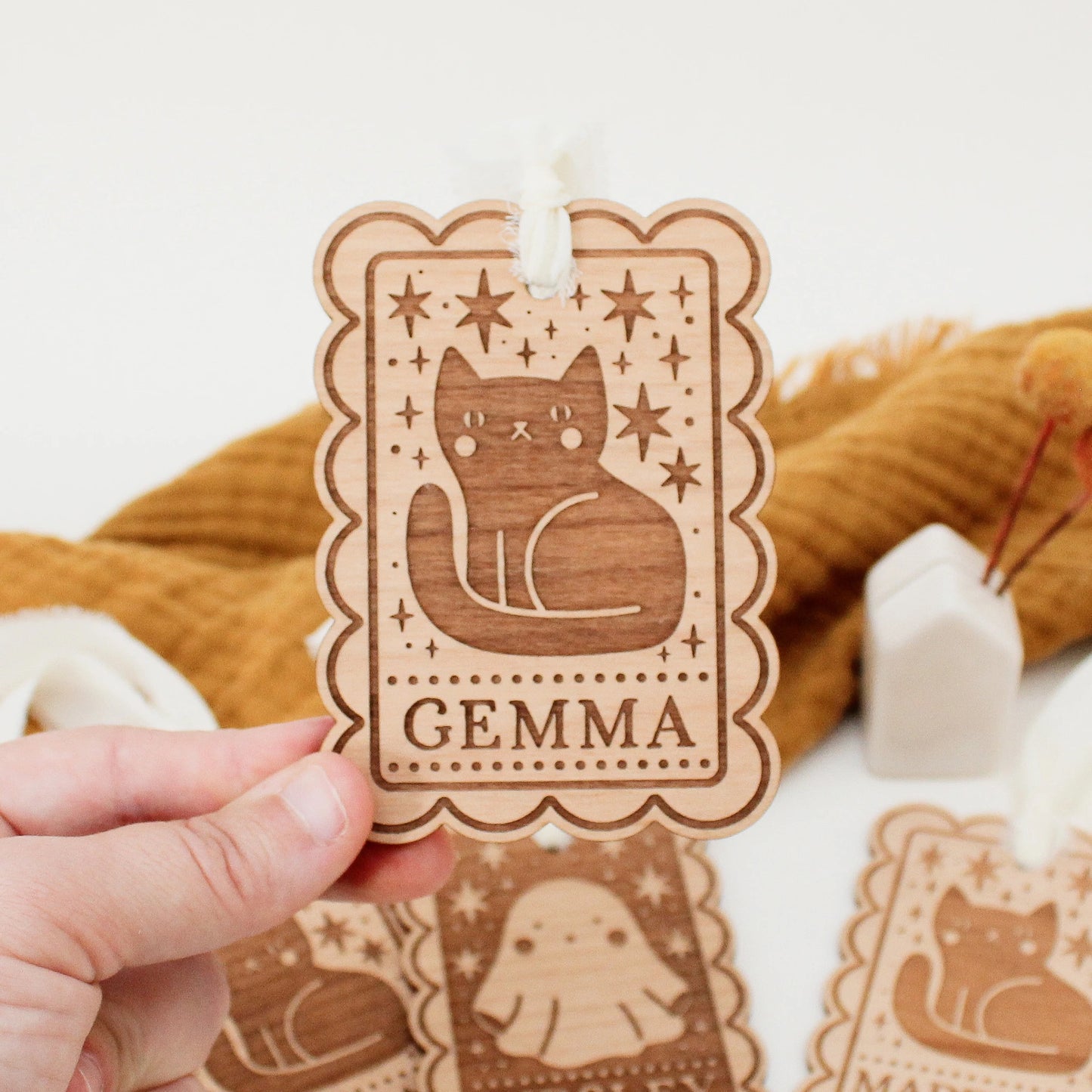 personalized halloween tag with black cat design being held in front of an orange blanket to show scale. tag is customized with the name GEMMA.