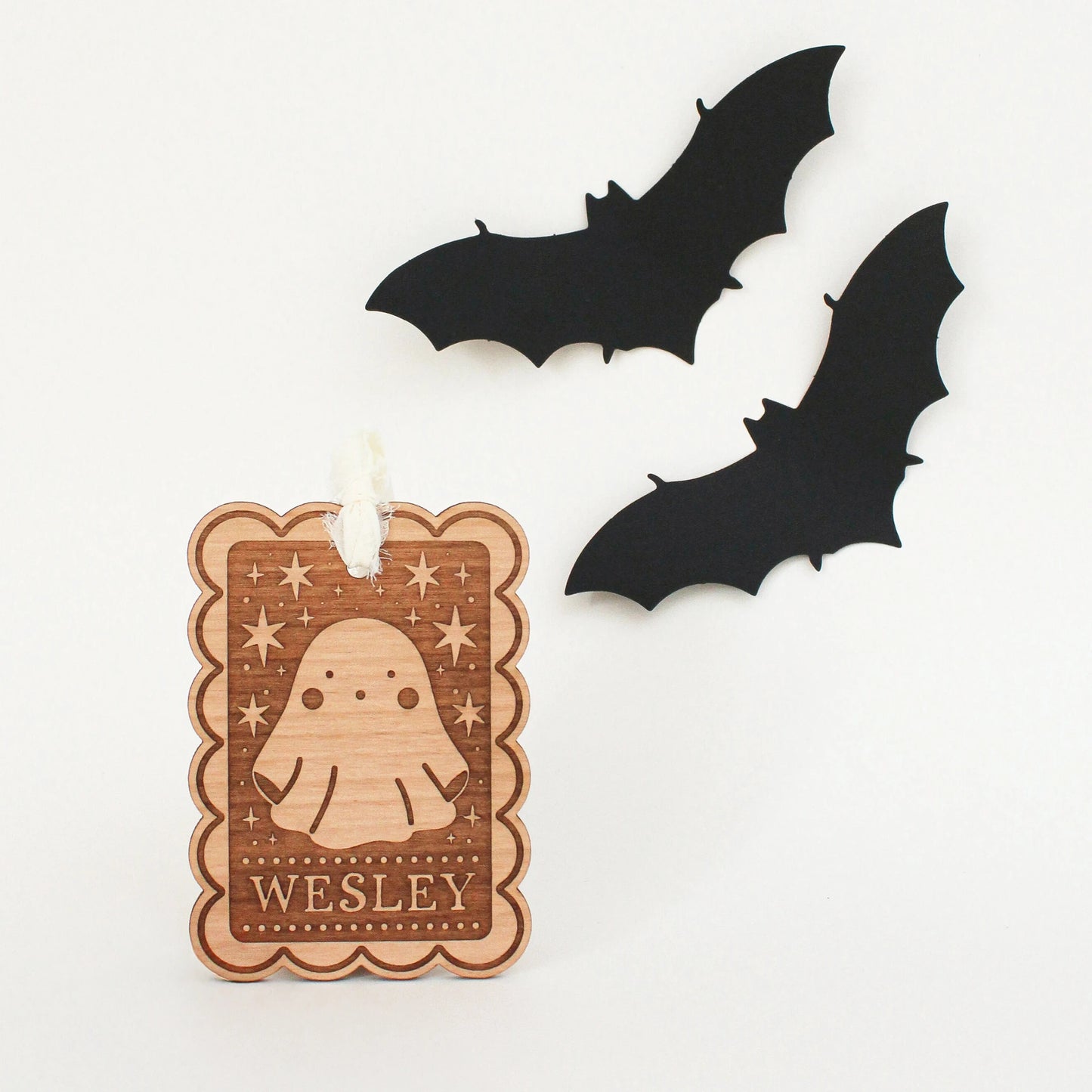 personalized halloween tags with ghost design propped up in front of white background with two black bats. tag is customized with the name WESLEY.
