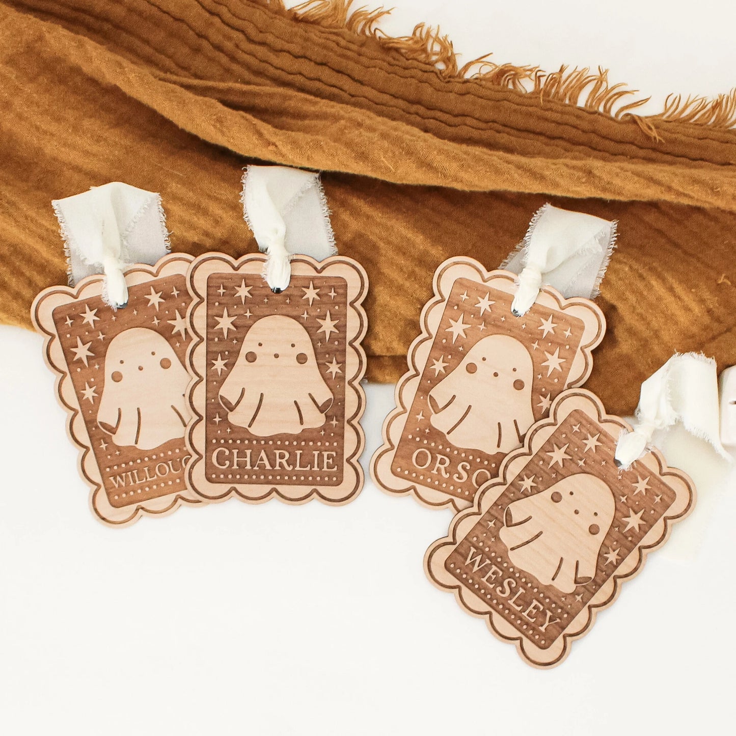 four personalized halloween tags with ghost designs laying in front of an orange blanket. tags are customized with names WILLOUGHBY, CHARLIE, ORSON, and WESLEY from left to right.