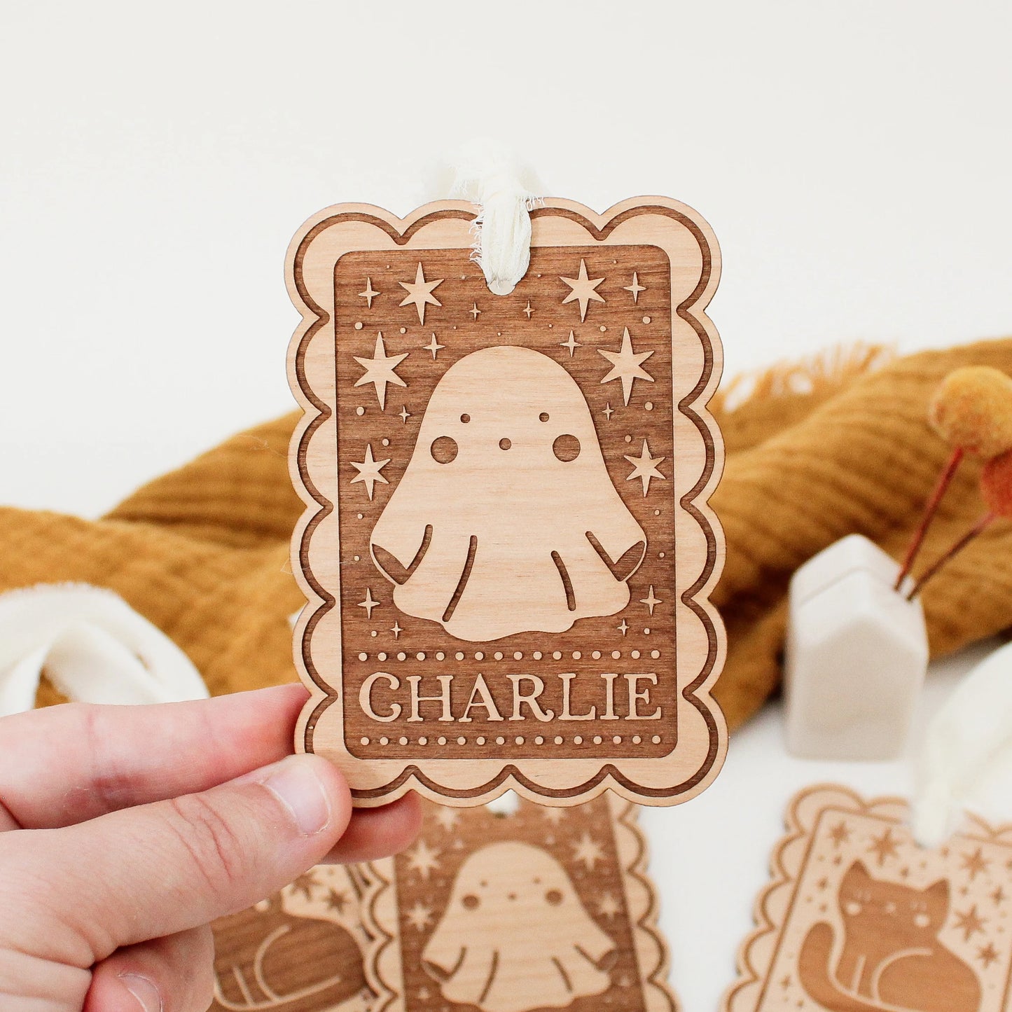 personalized halloween tag with ghost design being held in front of an orange blanket to show scale. tag is customized with the name CHARLIE.