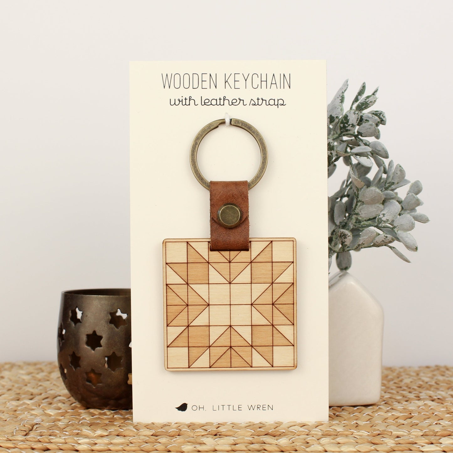 wooden keychain with quilt block pattern in two wood tones, with leather strap and bronze colored details.