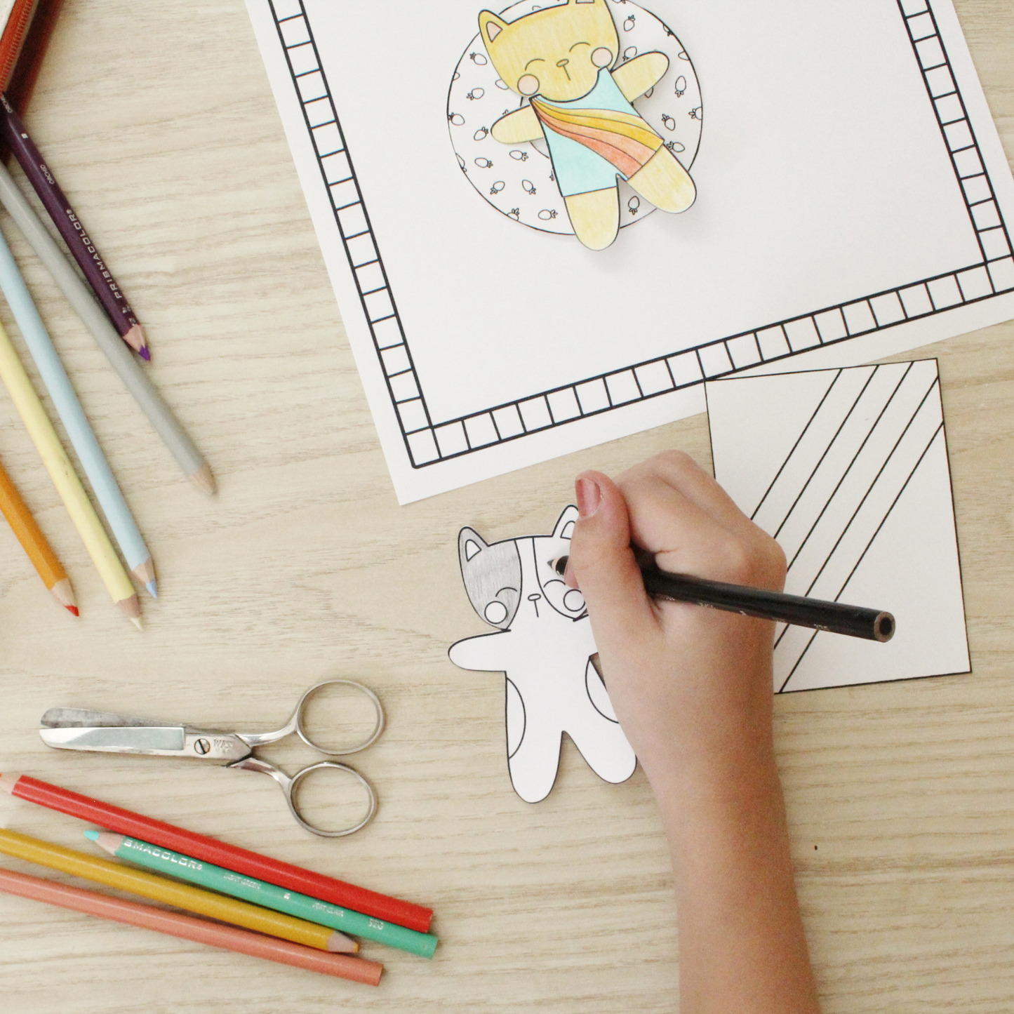 photo of a cat being colored. in the background is a cat floating on a strawberry float in a pool. there are colored pencils and scissors to the side.