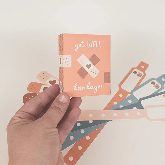 hand holding bandage box that says 'get well bandages' in the background are wristbands and bandages
