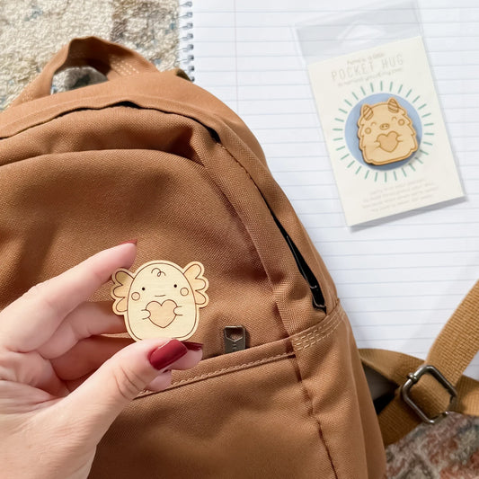 back to school wooden axolotl pocket hug is being placed into a backpack ready to calm first day of school nerves.