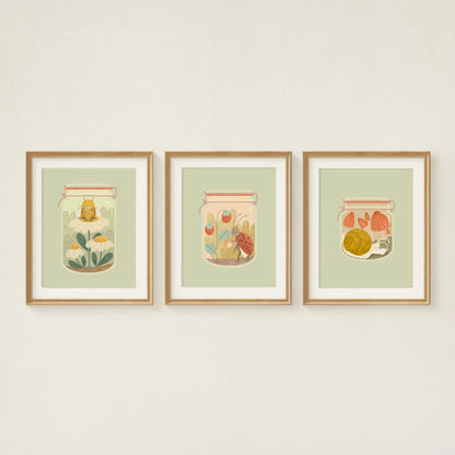 three art prints are shown hanging on the wall. from left to right: the bee's teas, tending to it, and slow afternoons. all feature insects in jars doing their cozy hobbies.