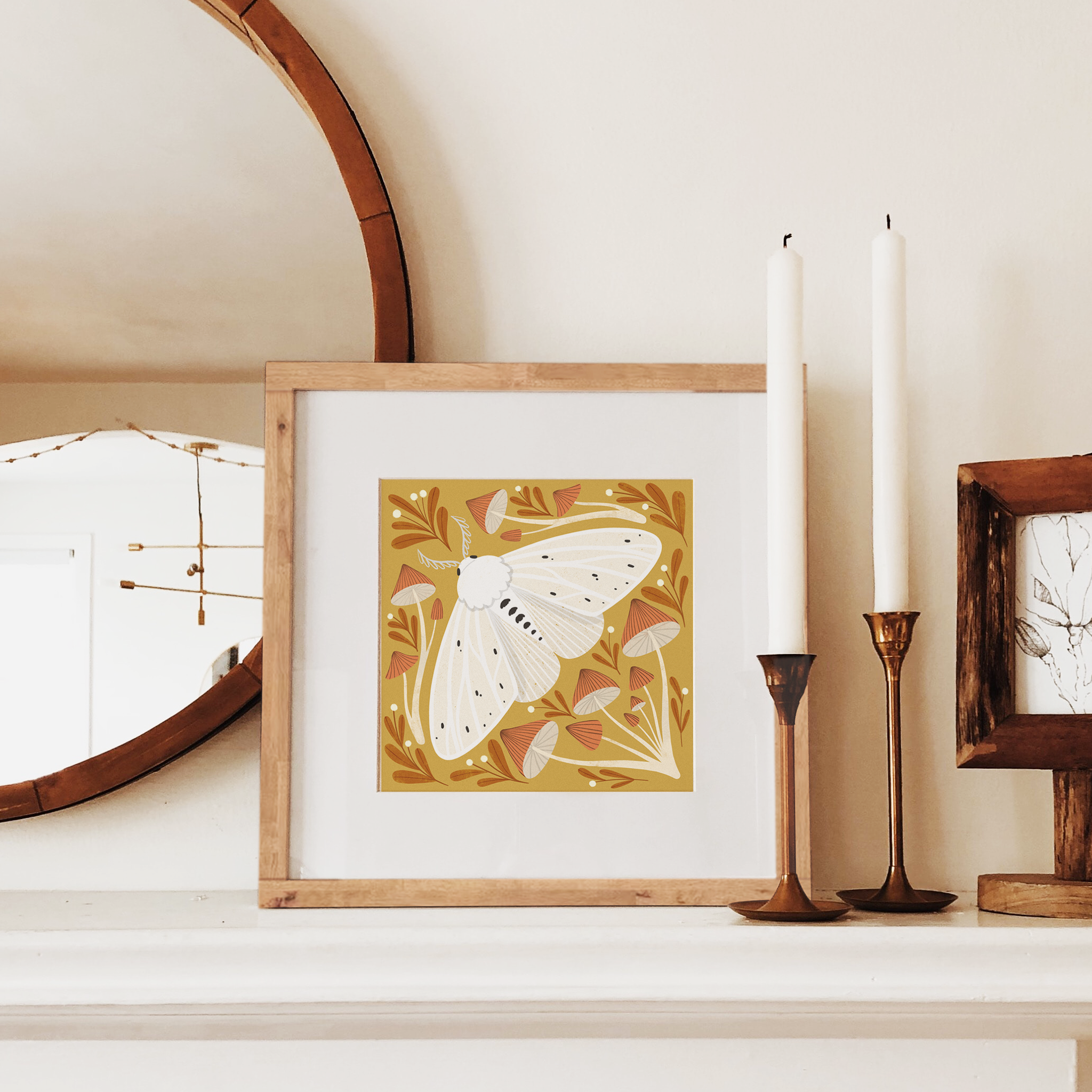 art print showing an agreeable tiger moth in black and white on a mustard yellow background, surrounded by red and white whimsical mushrooms. shown displayed in a wood frame, resting on a mantle.