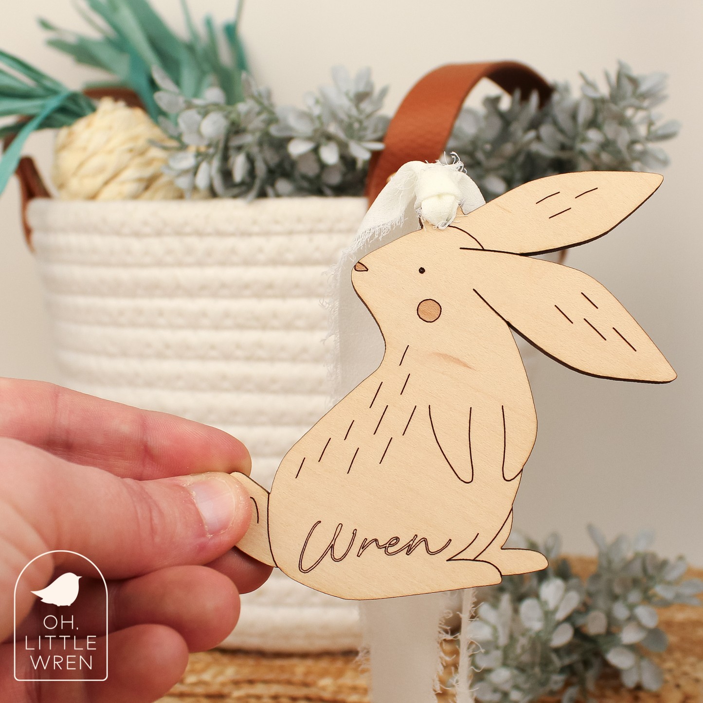 wooden easter bunny tag, being held by a hand. in maple wood tone with the name wren. shown in front of a white rope basket.
