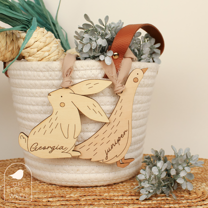 bunny and goose easter basket tags shown hanging from a white rope basket.