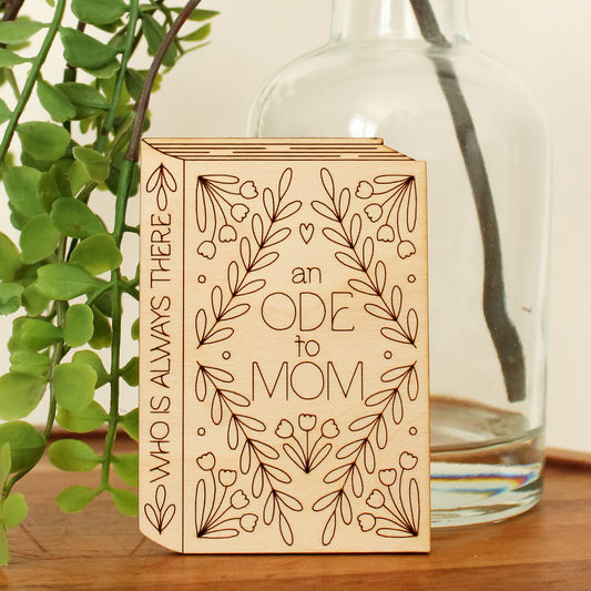 wooden book shaped card with floral motifs. cover reads 'an ode to mom'. spine reads 'who is always there'.