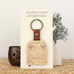 load image into gallery viewer, wooden keychain for the adventure lover. design has mountains, trees, fields and streams and the words &#39;adventure awaits&#39;.  wooden keychain with leather strap and bronze colored hardware.
