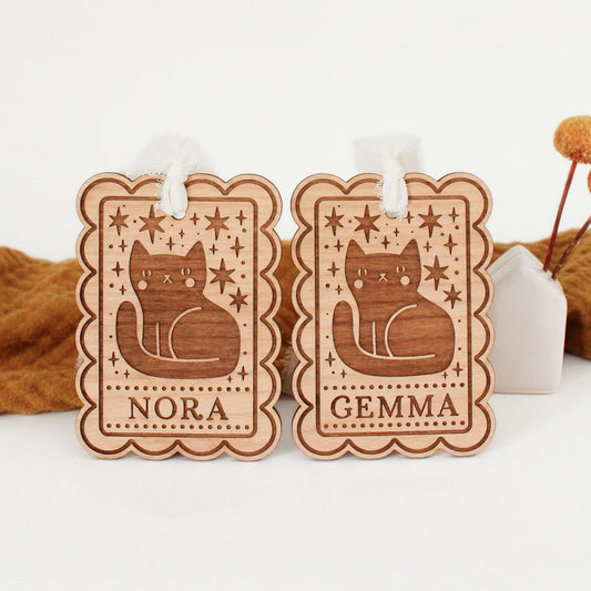 two personalized halloween tags with black cat designs propped up in front of an orange blanket. tags are customized with names NORA and GEMMA.