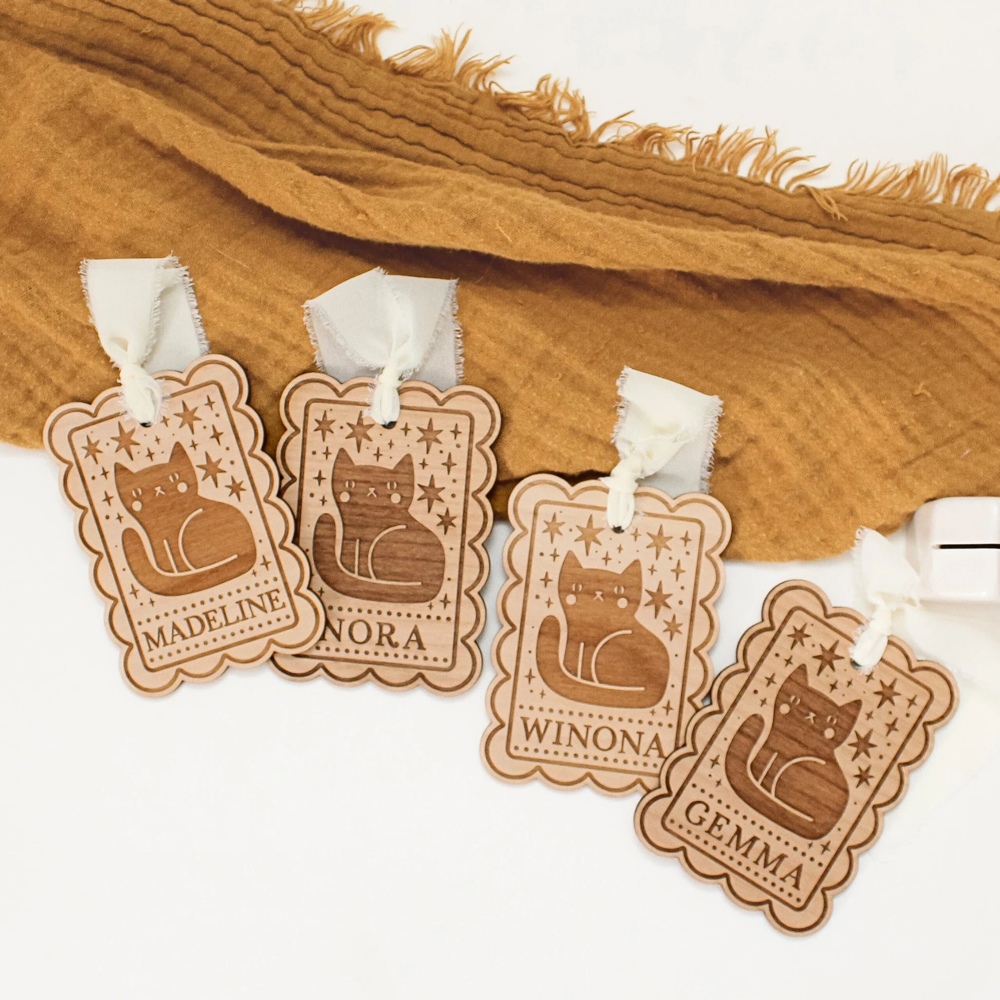 four personalized halloween tags with black cat designs laying in front of an orange blanket. tags are customized with names MADELINE, NORA, WINONA, and GEMMA from left to right.