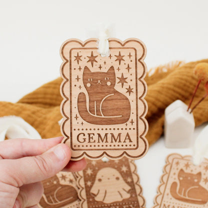 personalized halloween tag with black cat design being held in front of an orange blanket to show scale. tag is customized with the name GEMMA.