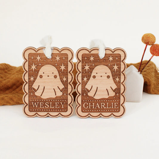 two personalized halloween tags with ghost designs propped up in front of an orange blanket. tags are customized with names WESLEY and CHARLIE.