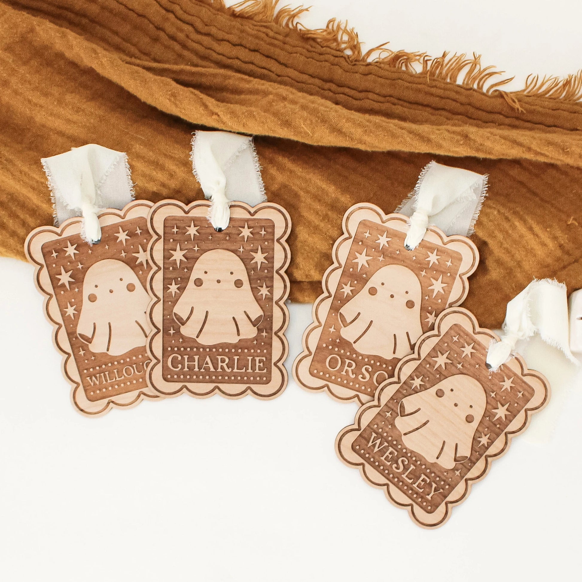 four personalized halloween tags with ghost designs laying in front of an orange blanket. tags are customized with names WILLOUGHBY, CHARLIE, ORSON, and WESLEY from left to right.
