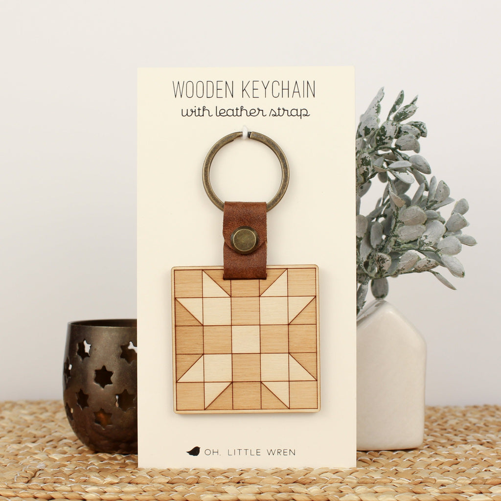 wooden keychain with quilt block pattern in two wood tones, with leather strap and bronze colored details.