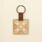 load image into gallery viewer, wooden keychain with quilt block pattern in two wood tones, with leather strap and bronze colored details.
