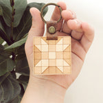 load image into gallery viewer, wooden keychain with quilt block pattern in two wood tones, with leather strap and bronze colored details.
