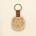 load image into gallery viewer, wooden keychain with snail design surrounded by mushrooms and the text &#39;it&#39;s ok to take it slow.&#39; with leather strap and bronze colored details.
