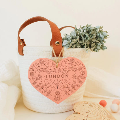 poppy pink colored heart with etched floral design and name, shown hanging from a basket. name reads LONDON.
