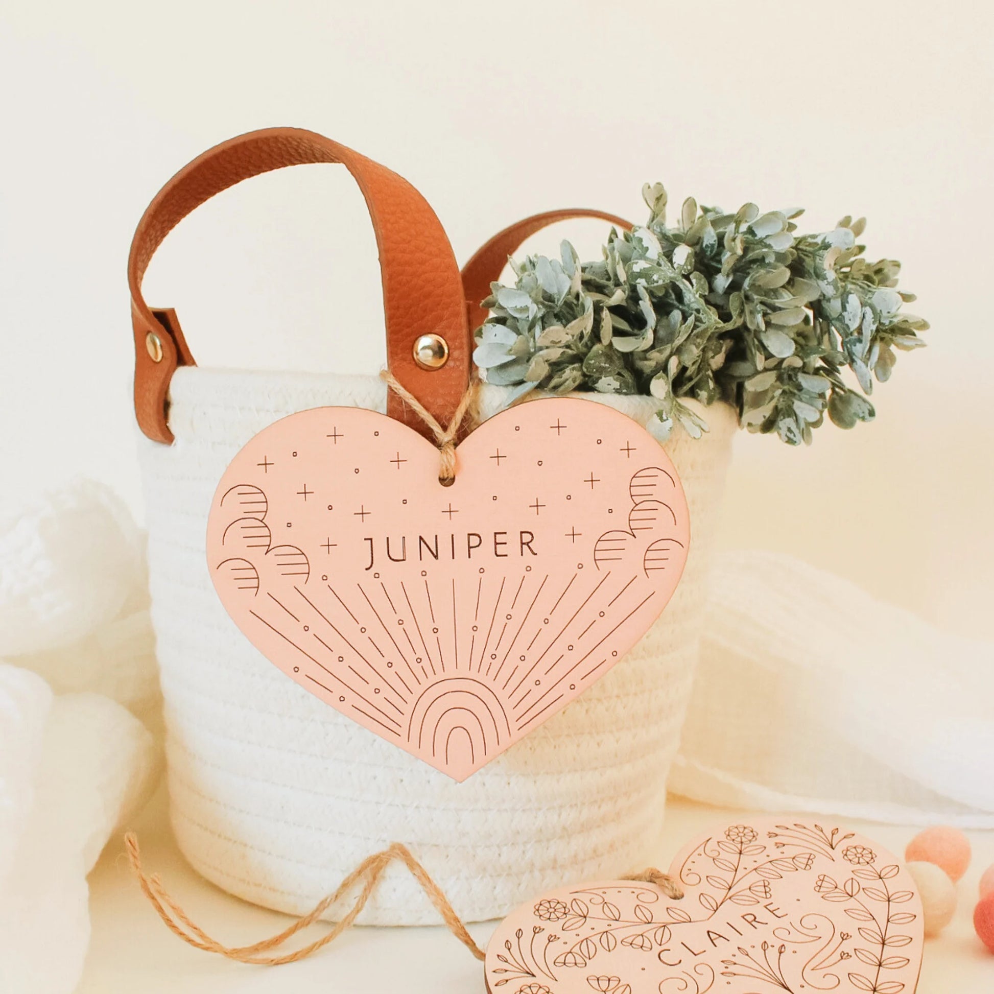 blush pink wood heart with etched rainbow and clouds design, shown hanging from a basket. name reads JUNIPER