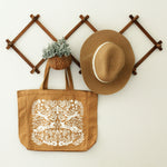 load image into gallery viewer, gusseted tote bag in burnt orange with a detailed silk screen design in warm white with florals, mushrooms, foxes, squirrels, rabbits and a bird. shown staged hanging on a wood accordion rack with a straw hat and greenery.
