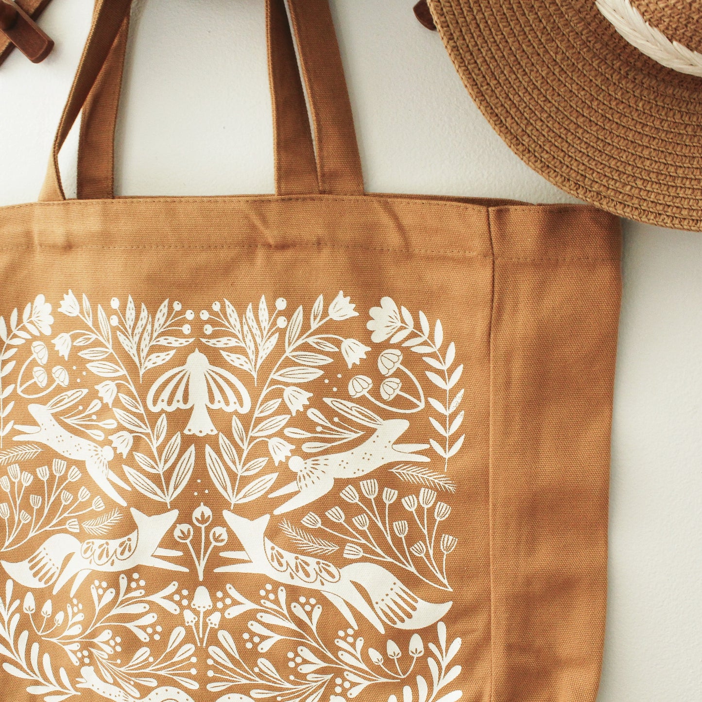 detailed shot of tote bag in burnt orange showing the detailed screen printed design of flowers, mushrooms and forest animals.