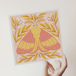 load image into gallery viewer, art print showing a rosy maple moth in bright pinks and yellows, surrounded by yellow and white whimsical florals. shown being held in a hand.
