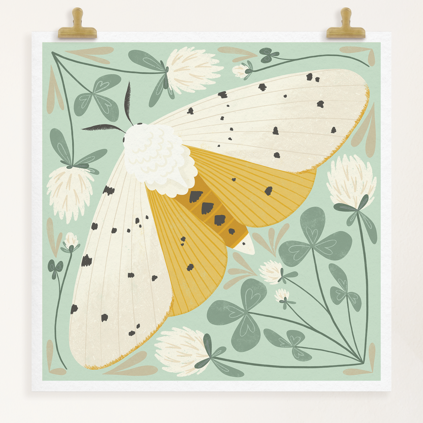 art print showing a salt marsh moth in black, white and mustard yellow, surrounded by whimsical mint green clovers and white clover flowers. shown displayed hanging from two gold clips.