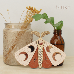 wooden moth with moon phase design. painted in blush pinks and terracotta reds with wood tones and mirrored rose gold moon phase inlays.