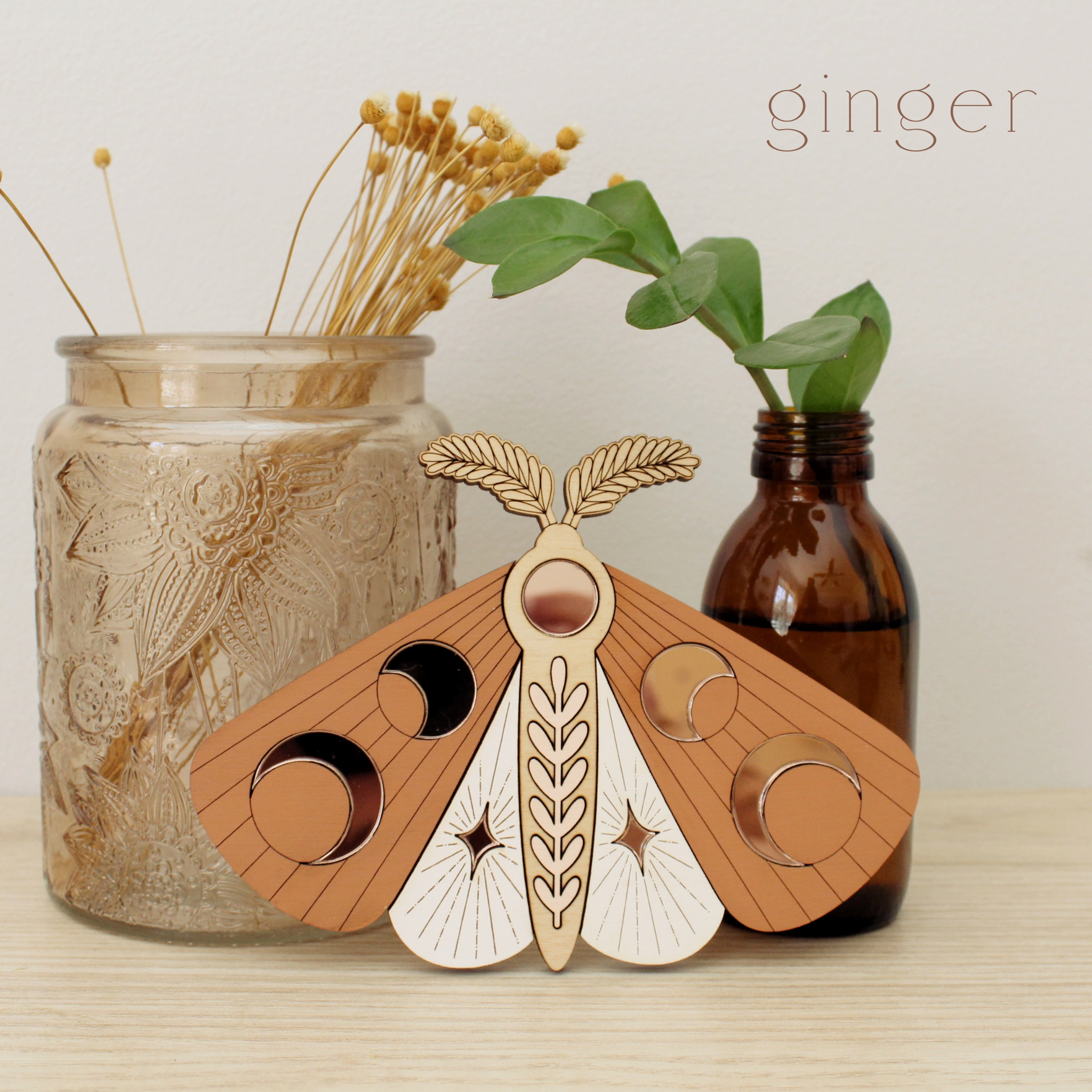 wooden moth with moon phase design. painted in orange and white with wood tones and mirrored rose gold moon phase inlays.