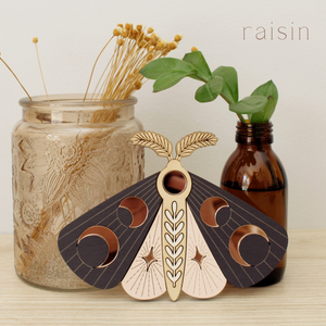 wooden moth with moon phase design. painted in blush pinks and deep plum with wood tones and mirrored rose gold moon phase inlays.