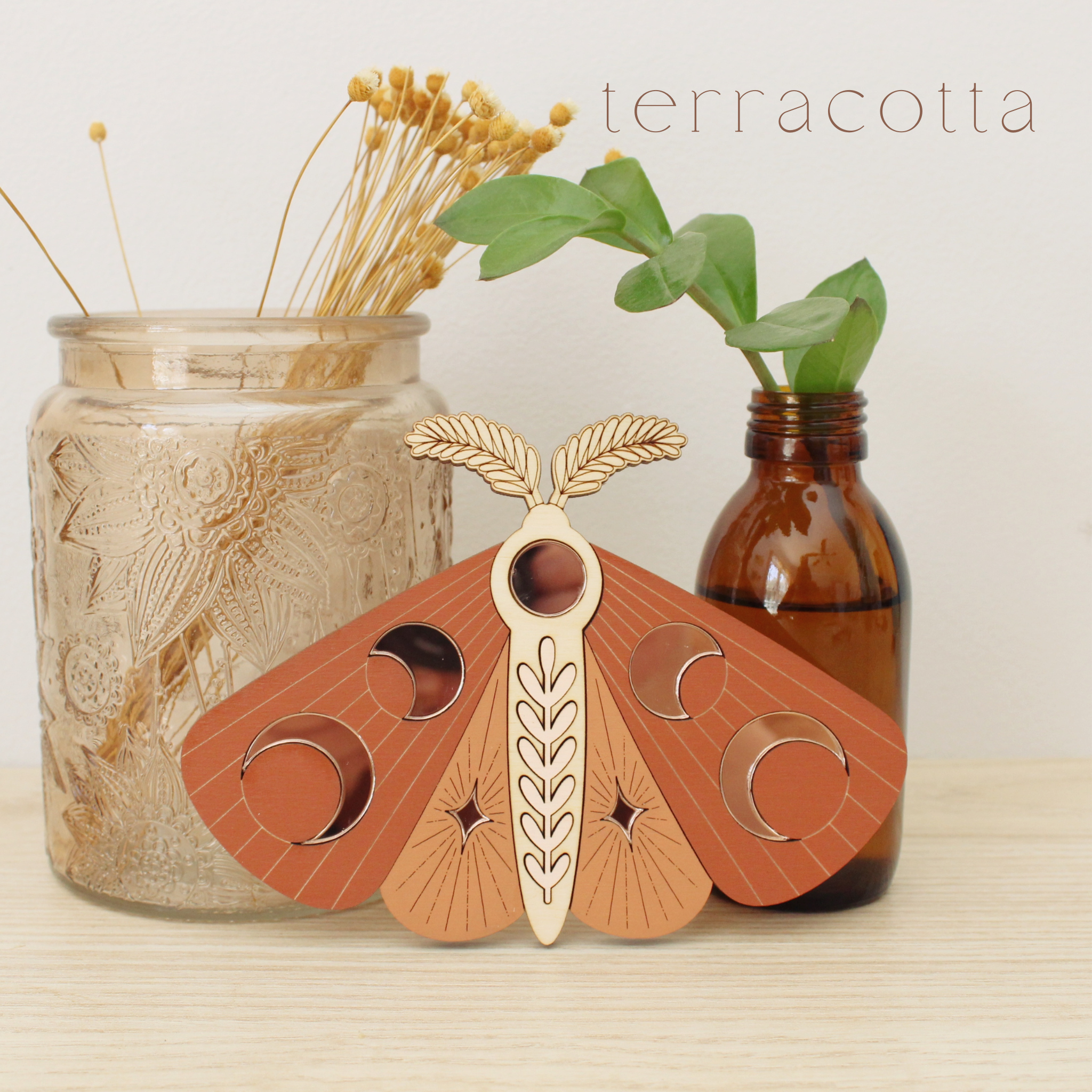 wooden moth with moon phase design. painted in orange and terracotta reds with wood tones and mirrored rose gold moon phase inlays.