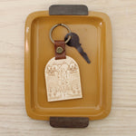 load image into gallery viewer, wooden keychain for the adventure lover. design has mountains, trees, fields and streams and the words &#39;adventure awaits&#39;.  wooden keychain with leather strap and bronze colored hardware.
