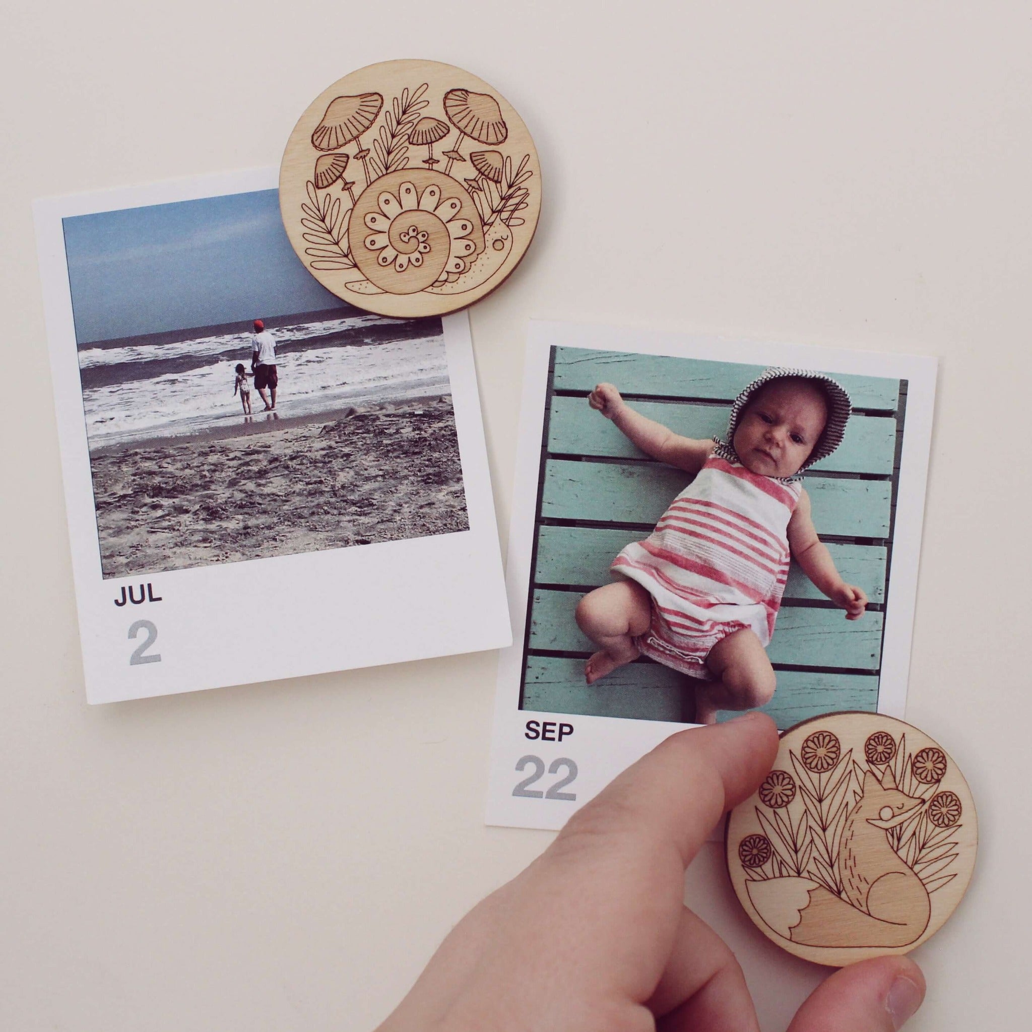 pair of circular wooden magnets, one with a fox surrounded by flowers and the other with a snail and mushrooms.