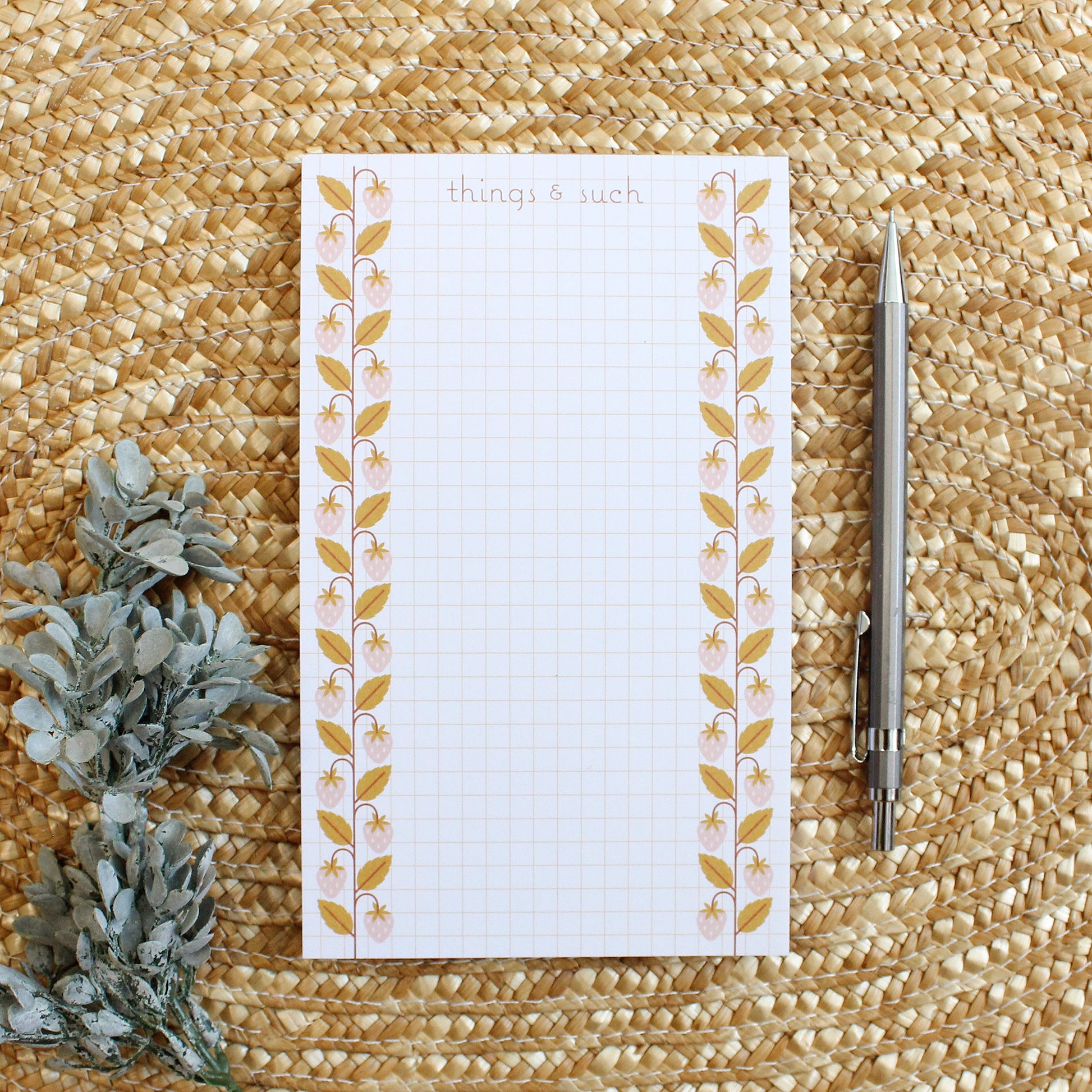 grid lined notepad with pink strawberries with mustard leaves going up each side.