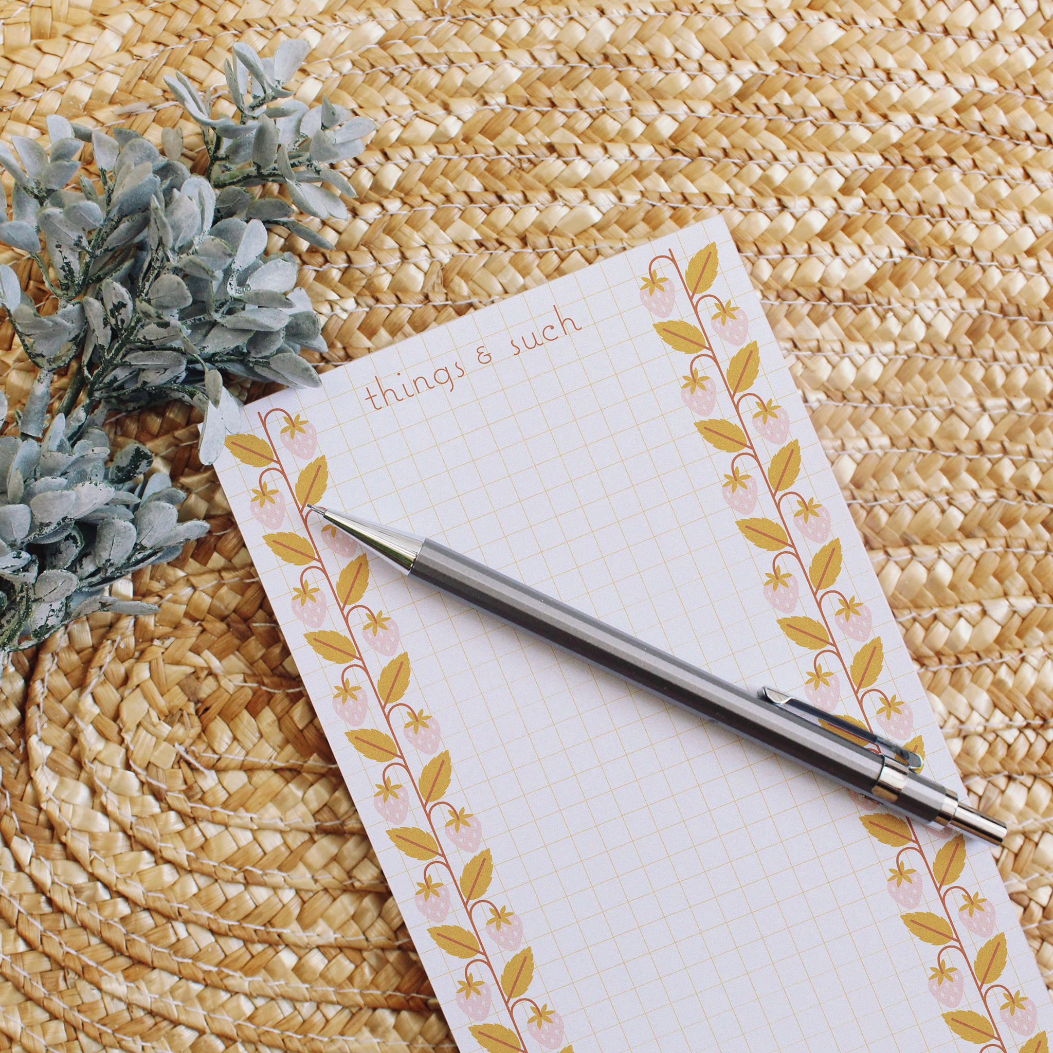 grid lined notepad with pink strawberries with mustard leaves going up each side.